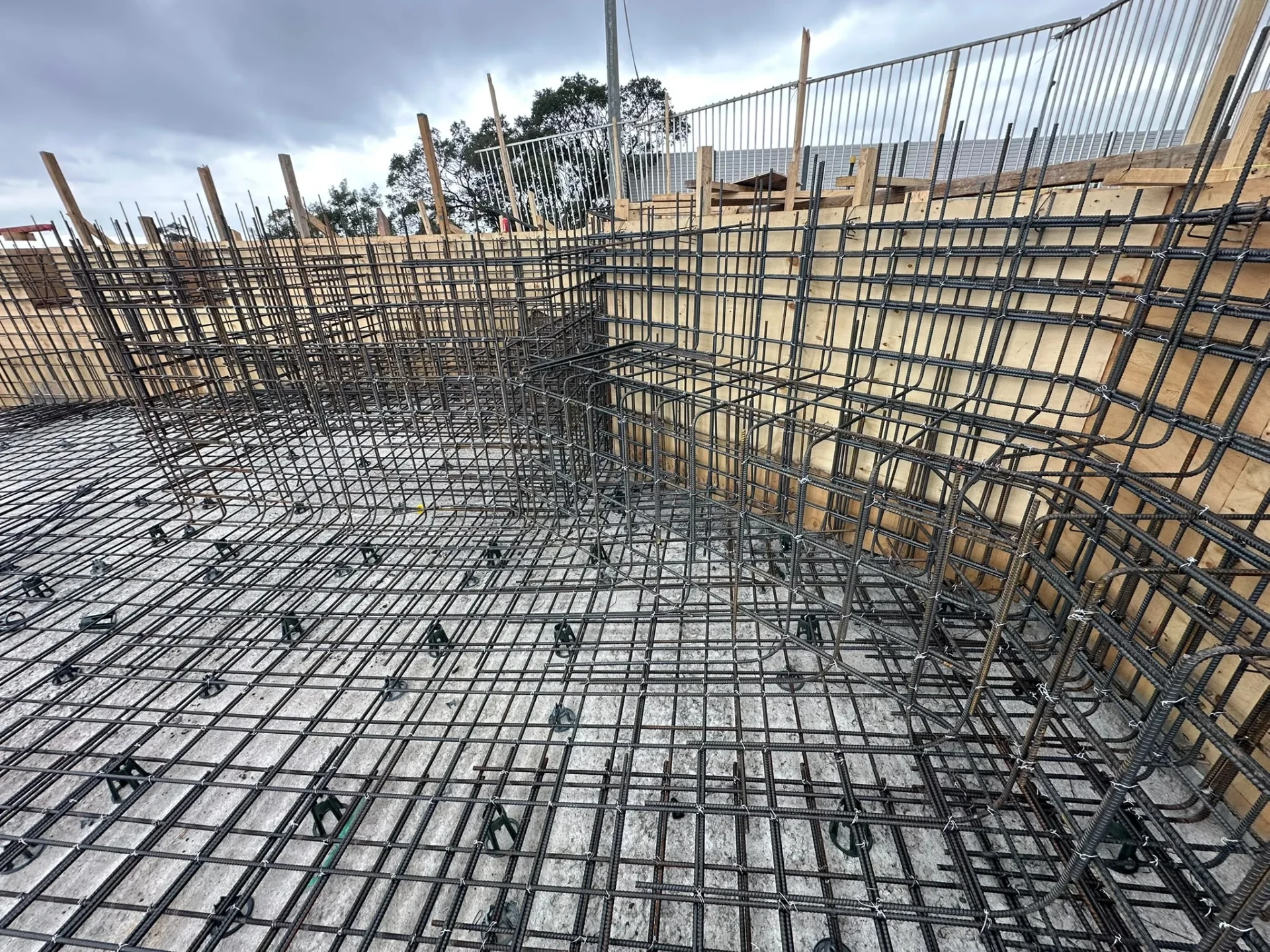 Pool excavation lined with plywood formwork, with wall reinforcement cages and floor steel tied over a blinding layer.